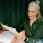 Starsza kobieta w okularach czyta dokumenty przy biurku