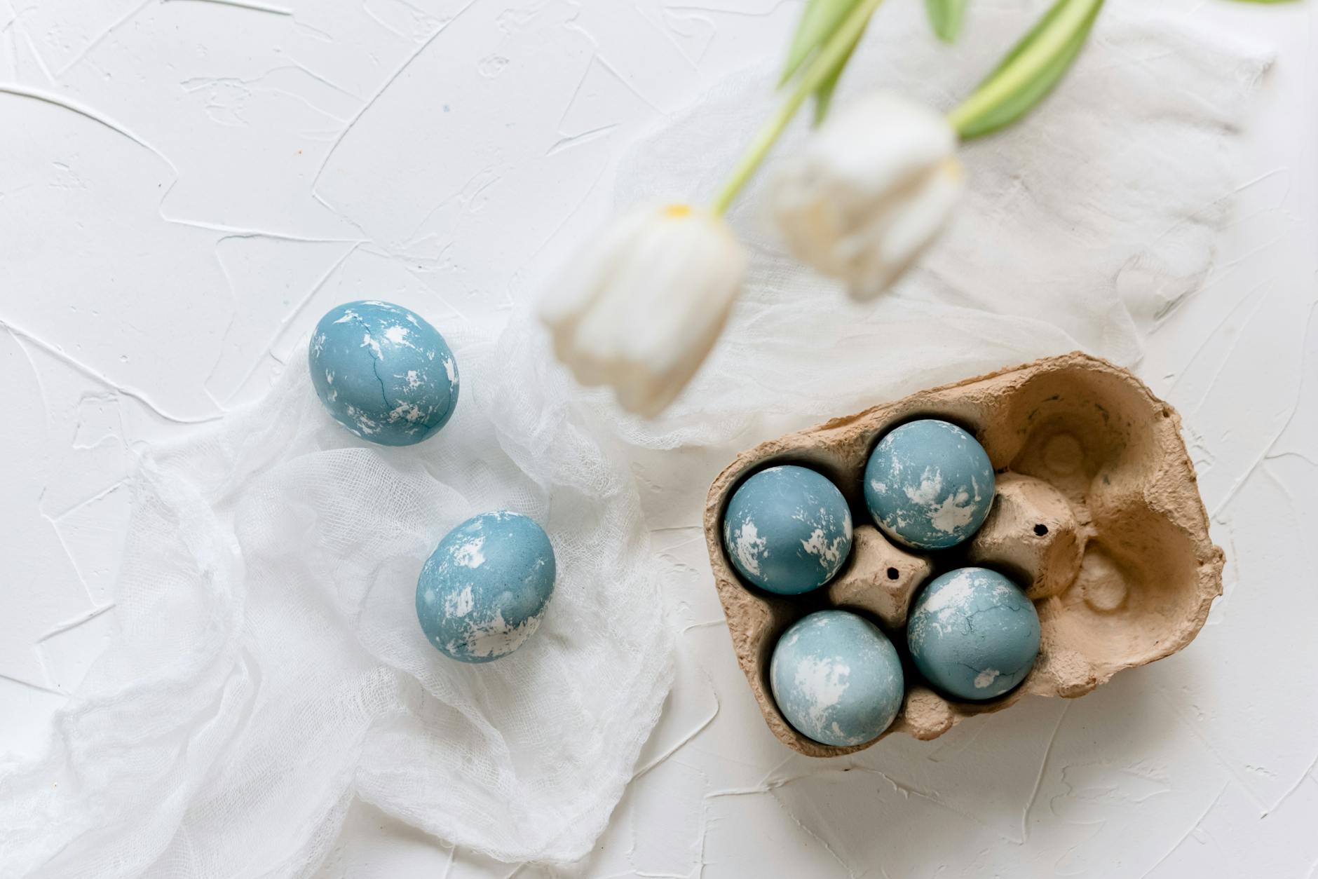 Niebieskie marmurkowe pisanki wielkanocne obok białych tulipanów