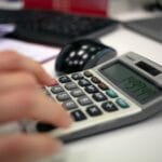 Czy zakonnik może mieć pracę świecką? Zasady i realia życia konsekrowanego Dłoń zakonnika licząca na kalkulatorze przy biurku w biurze