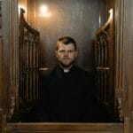 Kapłan siedzący poważnie w drewnianej konfesjonale w kościele
