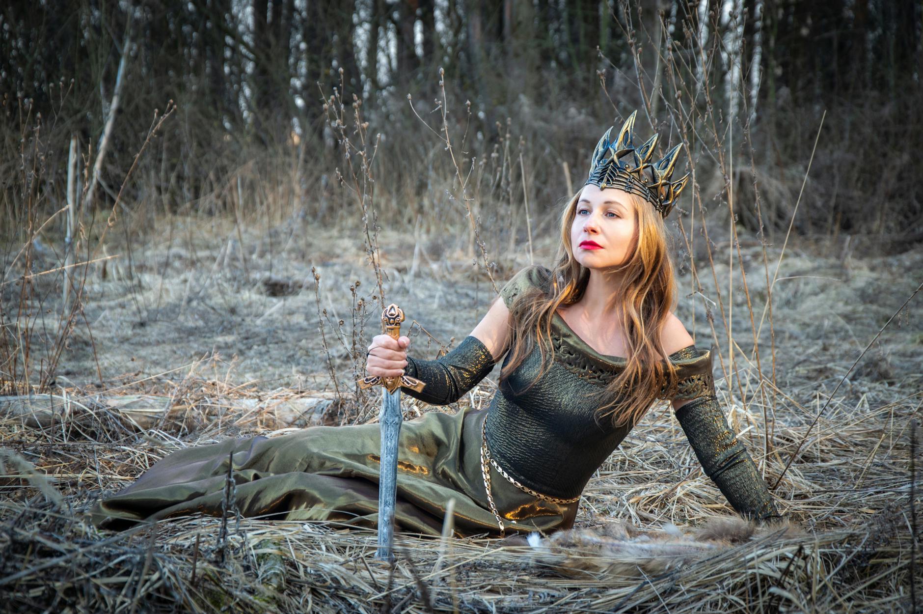 Kobieta w zbroi i koronie z mieczem w ręku w tajemniczym lesie