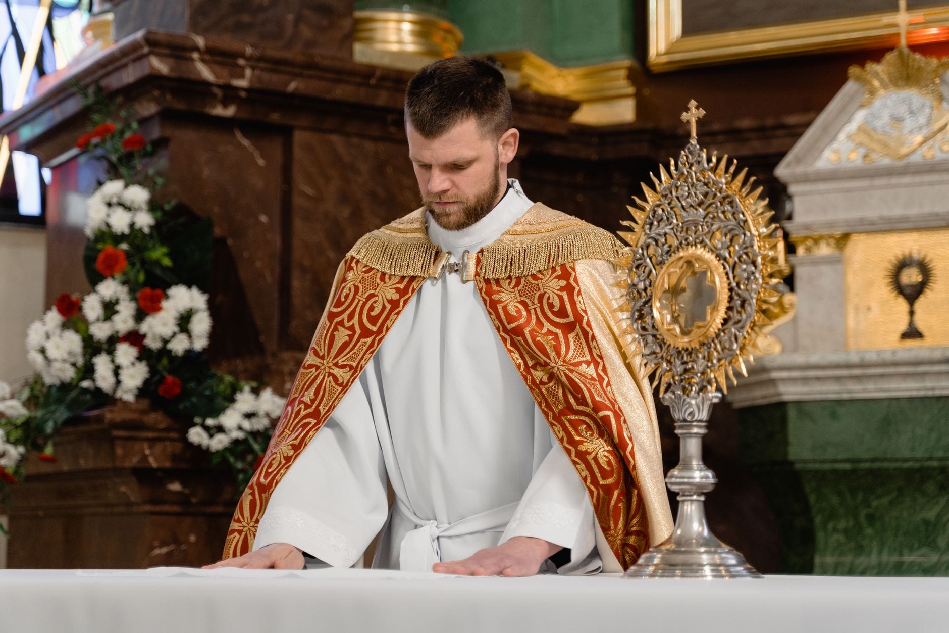 Kapłan modli się przy Eucharystii na ołtarzu udekorowanym kwiatami