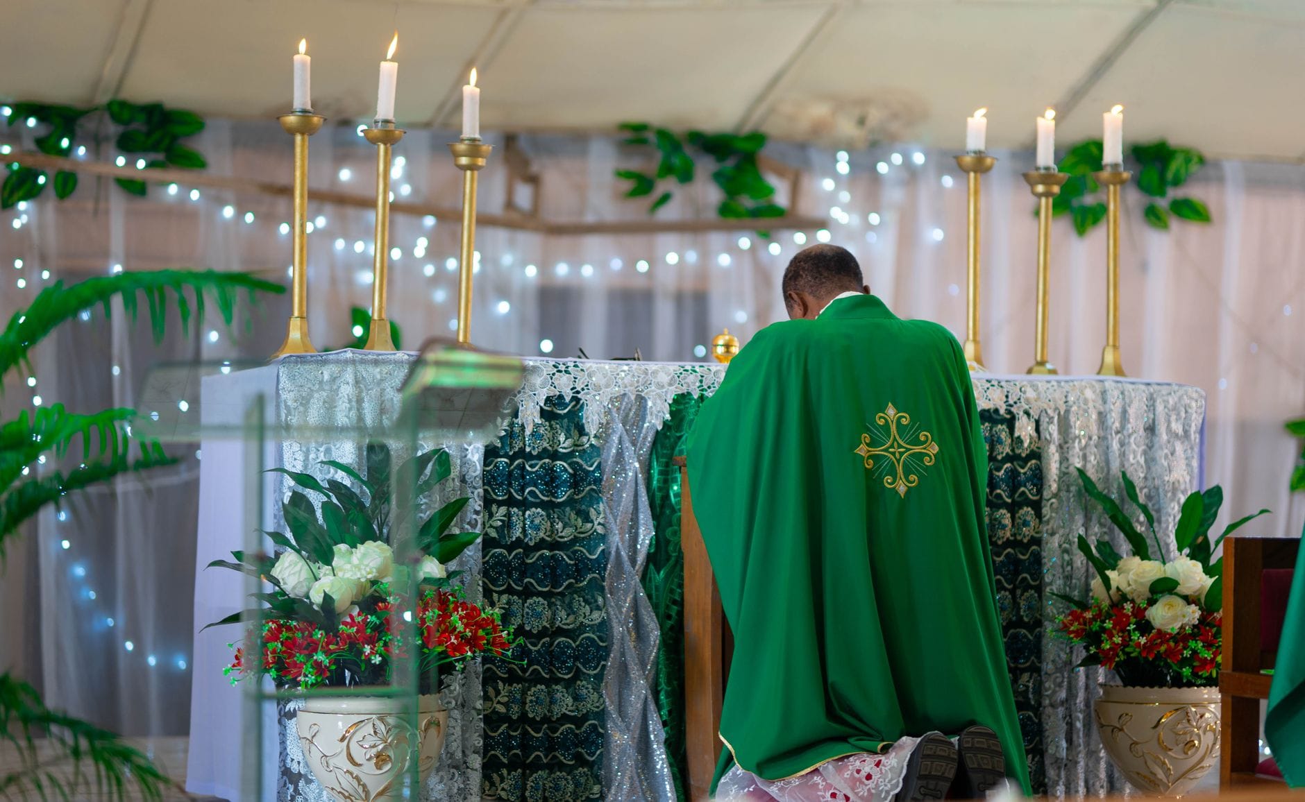 Kapłan w zielonych szatach modli się przy ołtarzu z zapalonymi świecami